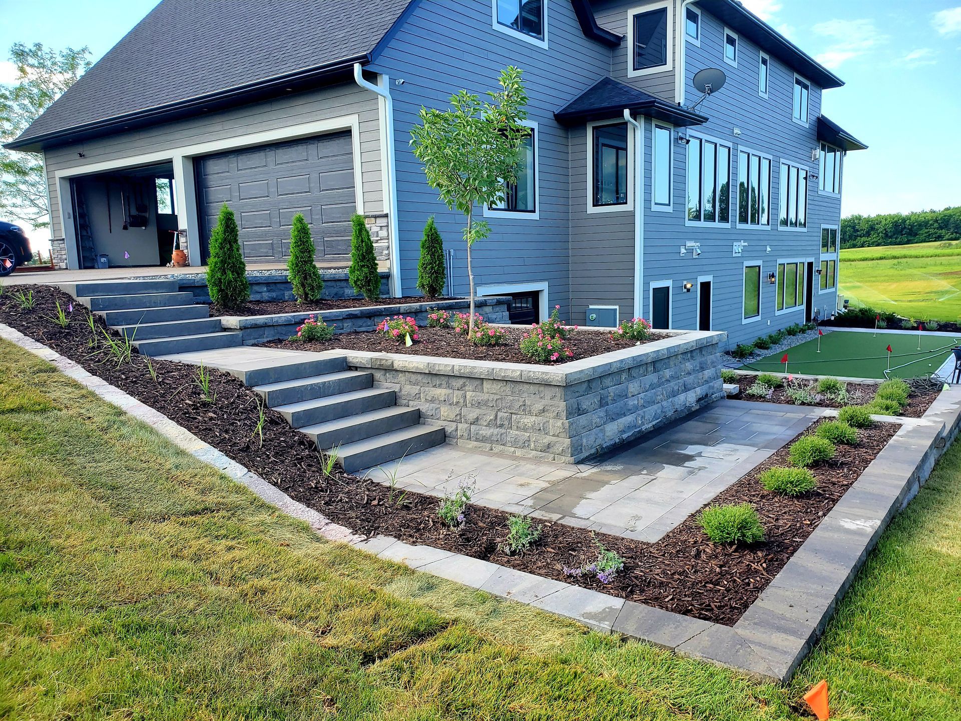 Multi-level backyard landscaping with retaining walls, steps, and patio near a gray house.