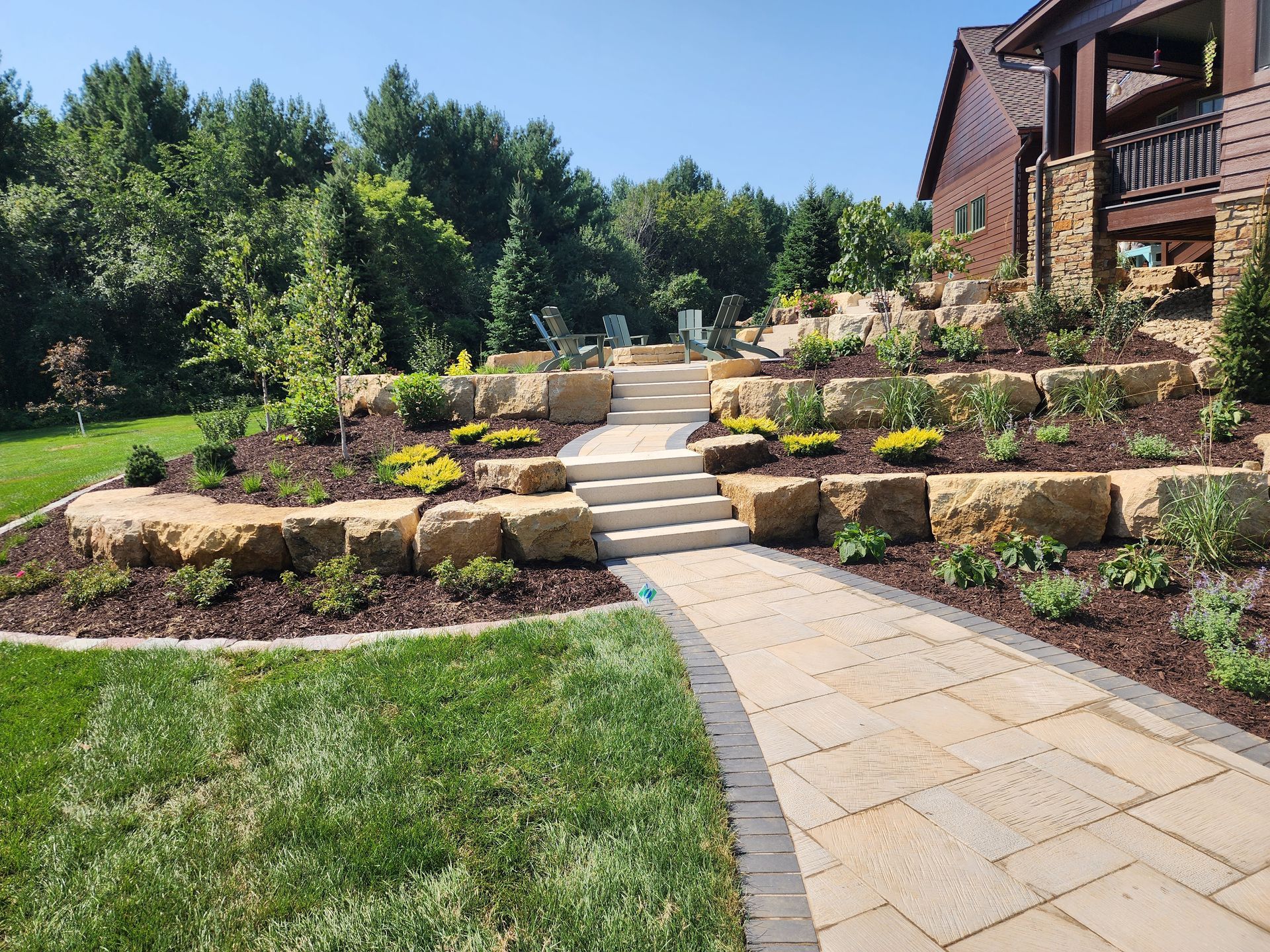 Stone pathway and steps lead up a terraced garden with greenery and a house in the background.
