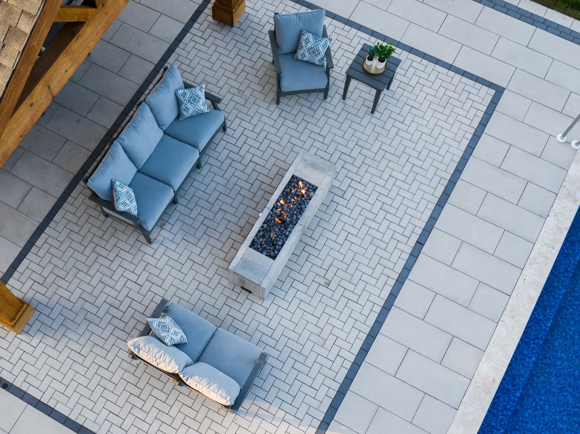 Patio with blue seating, fire pit, and small table on stone pavers. Pool visible.