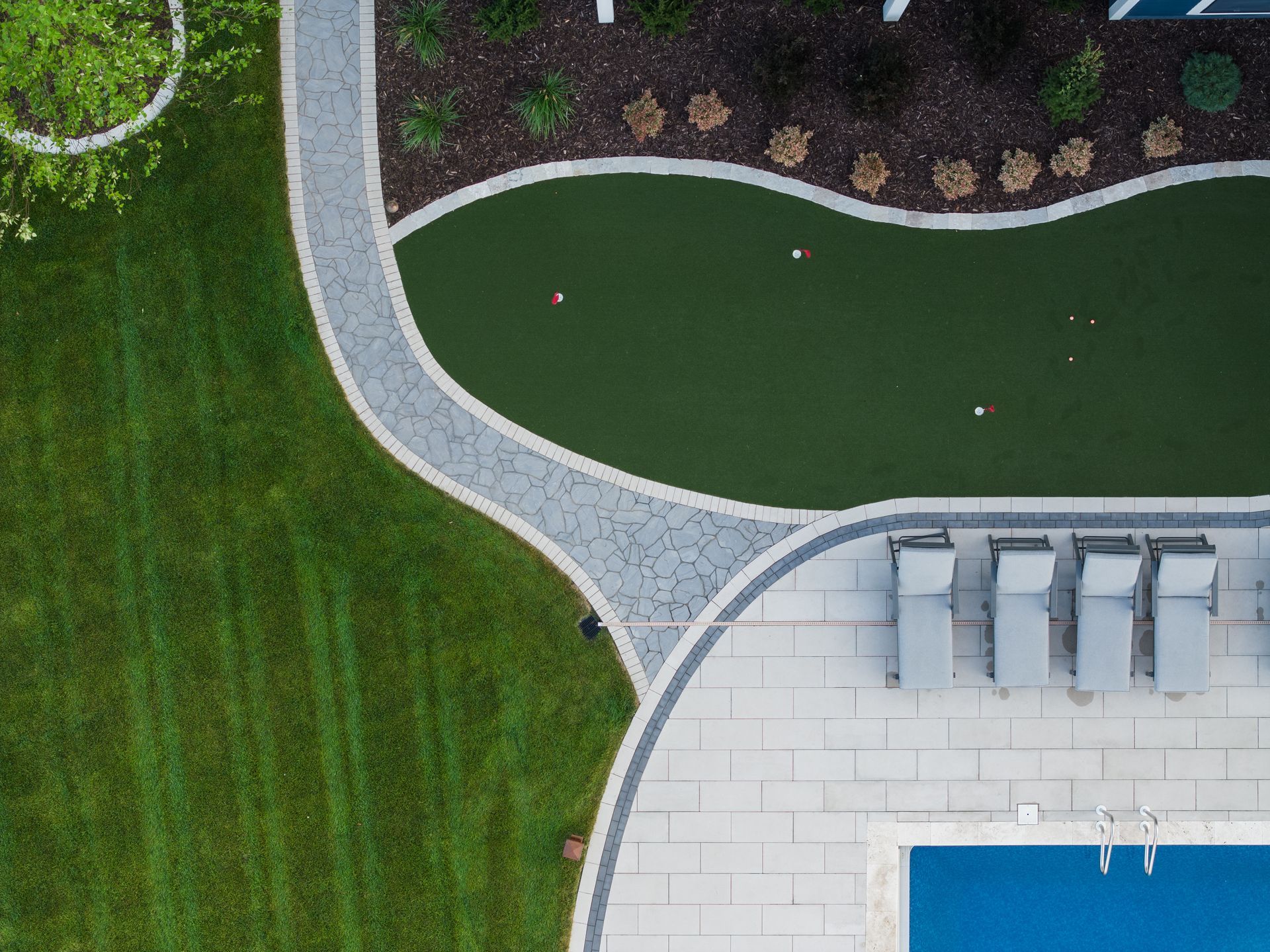 Aerial view of backyard with putting green, pool, lounge chairs, and path.