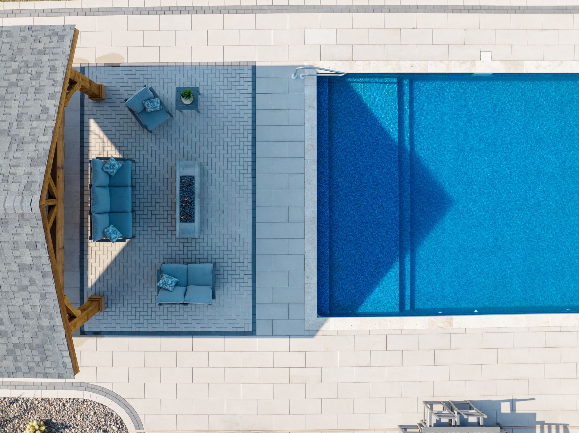 Overhead view of a rectangular pool with blue water next to a patio with outdoor furniture under a wooden pergola.