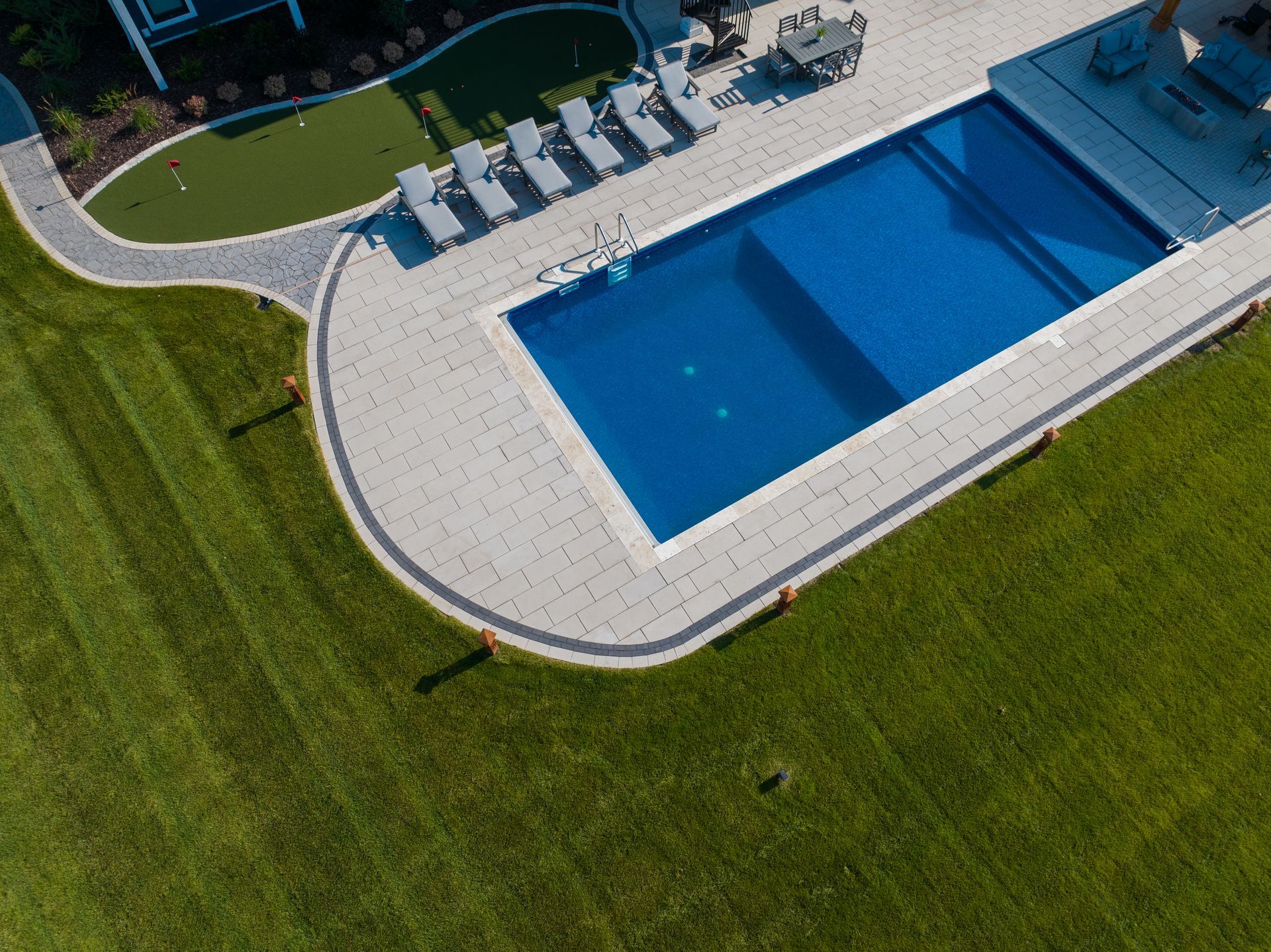 Aerial view of a rectangular blue swimming pool surrounded by a stone patio and green lawn.