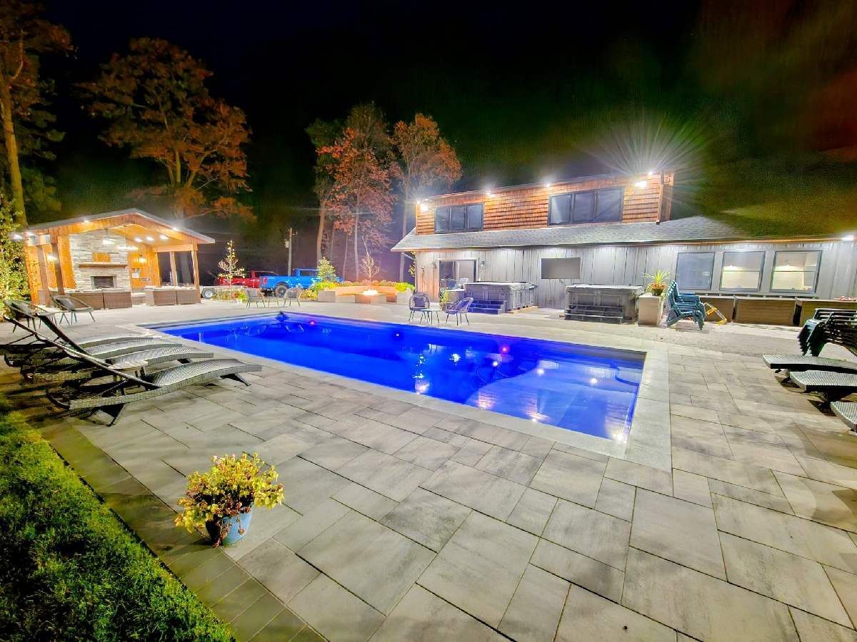 A large swimming pool is in the backyard of a house at night.