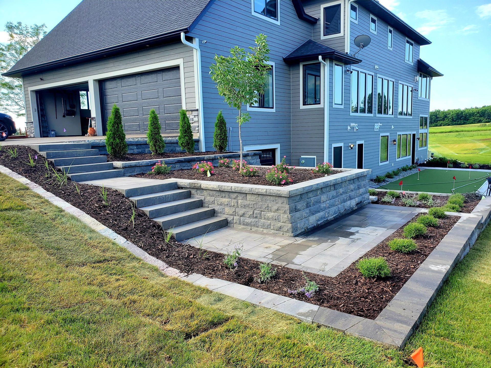 A large house with stairs leading up to it and a lush green yard in front of it.