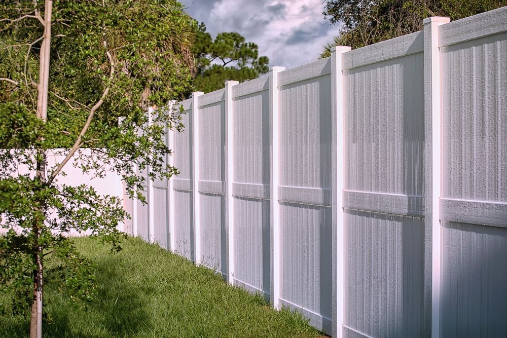 A white fence is surrounded by grass and trees in a backyard.
