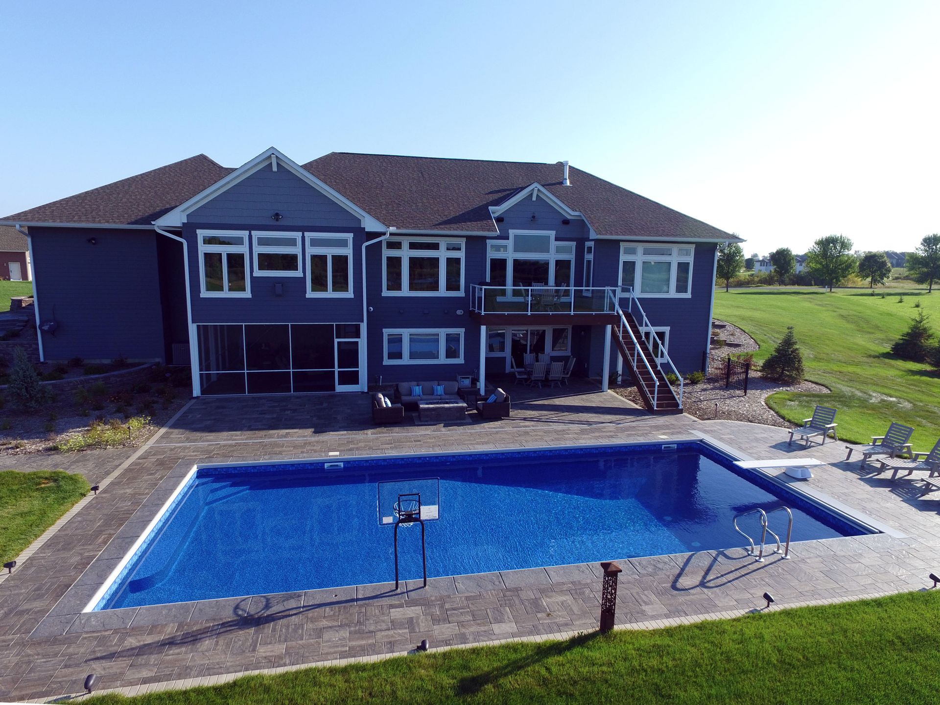 Blue house with a backyard swimming pool and green lawn on a sunny day.