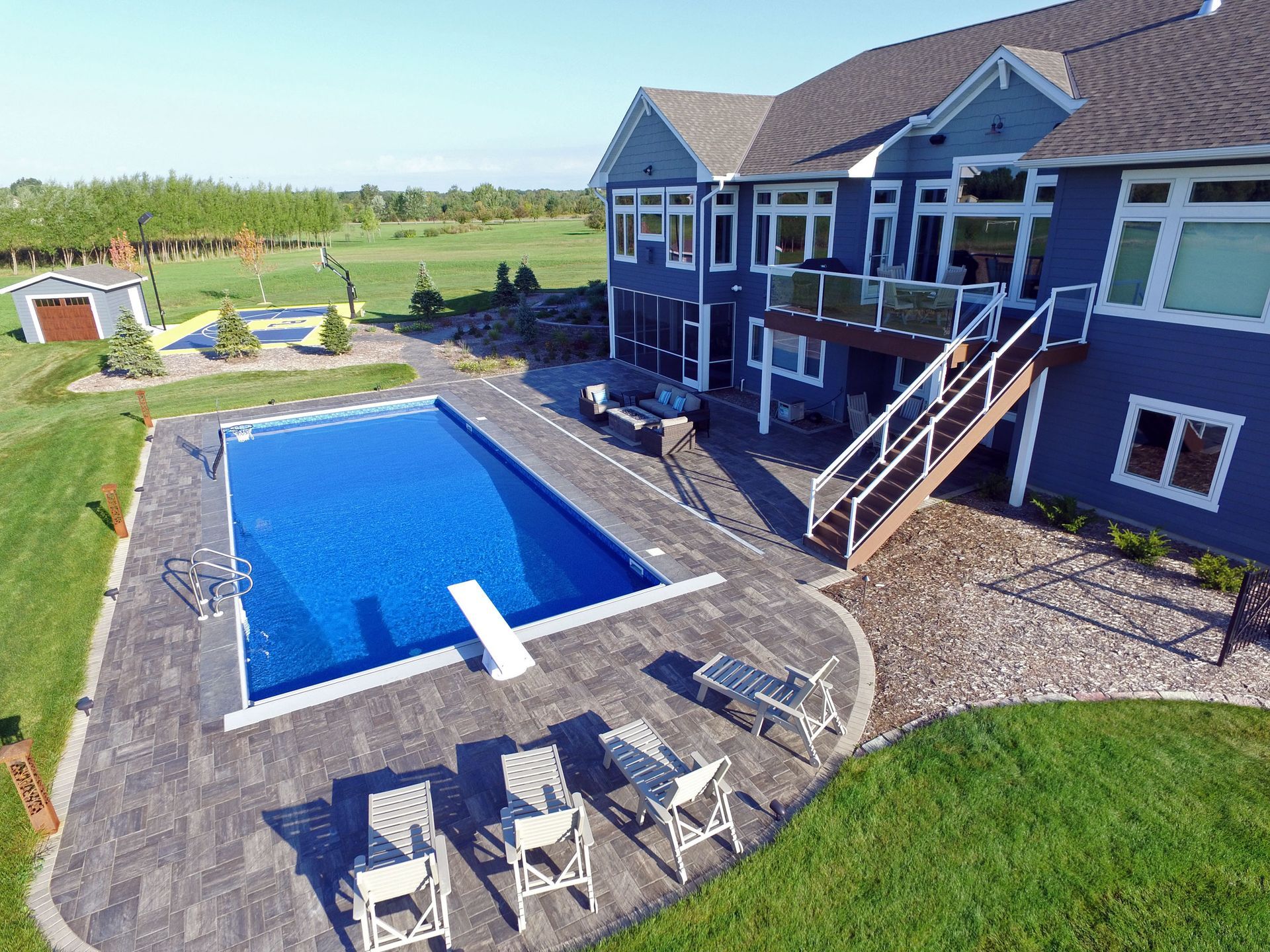 Blue house with a rectangular pool, diving board, and lounge chairs on a paved patio.
