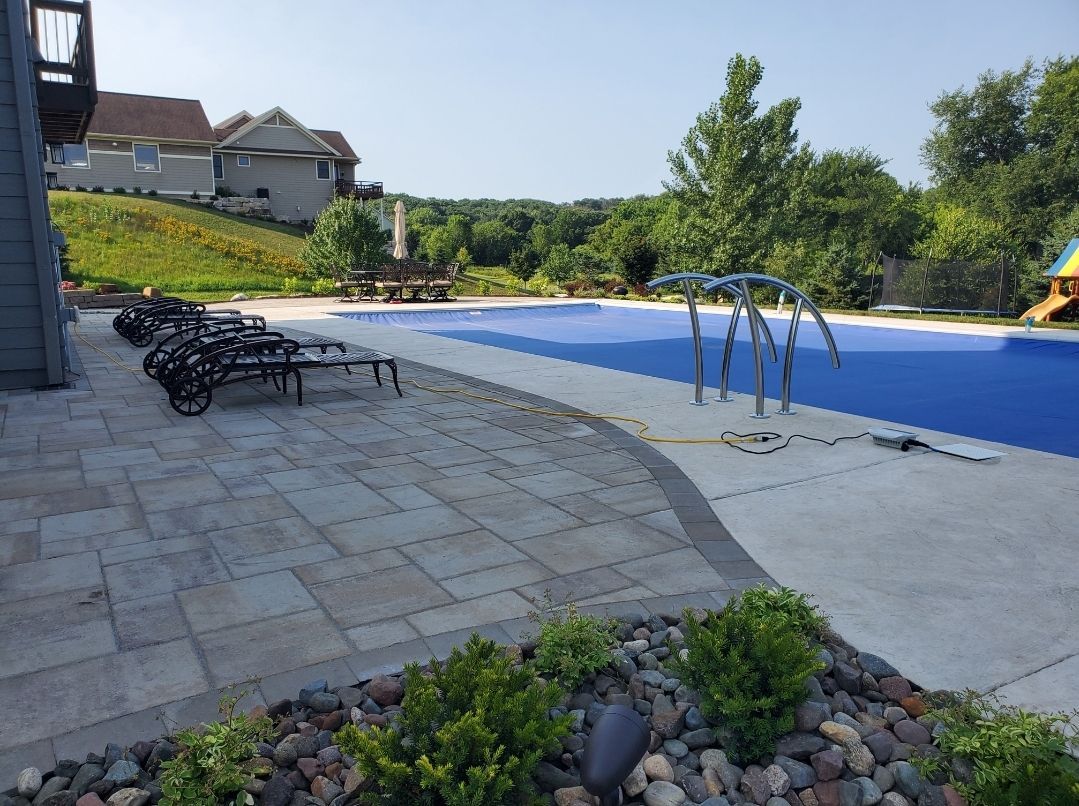 Patio with pool covered in blue; lounge chairs, landscaping and a house in the background.