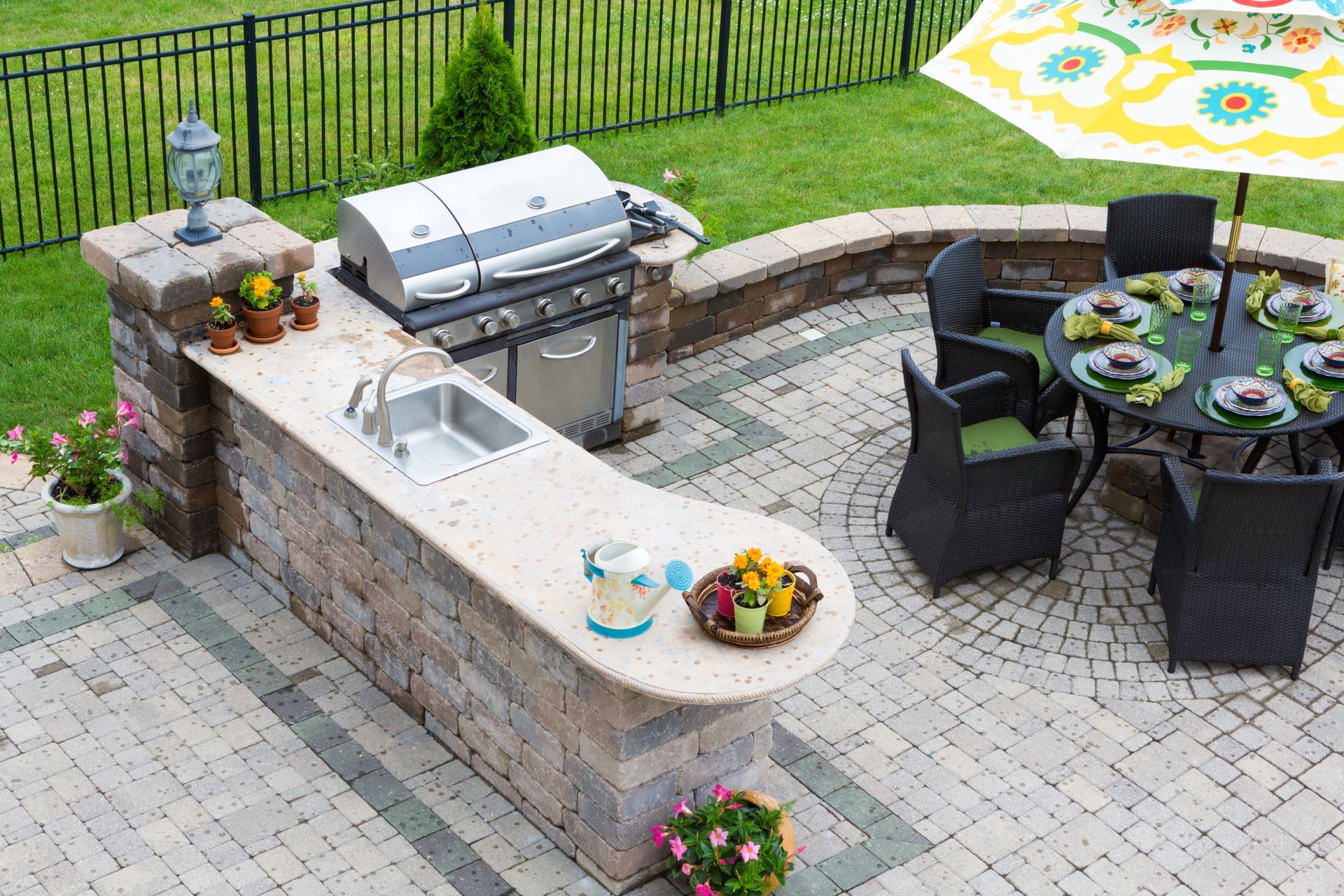 An outdoor kitchen with a grill , sink , table and chairs.