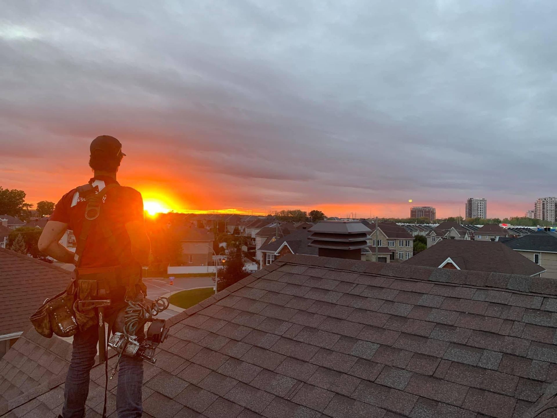 Un homme se tient debout sur un toit et regarde le coucher du soleil.