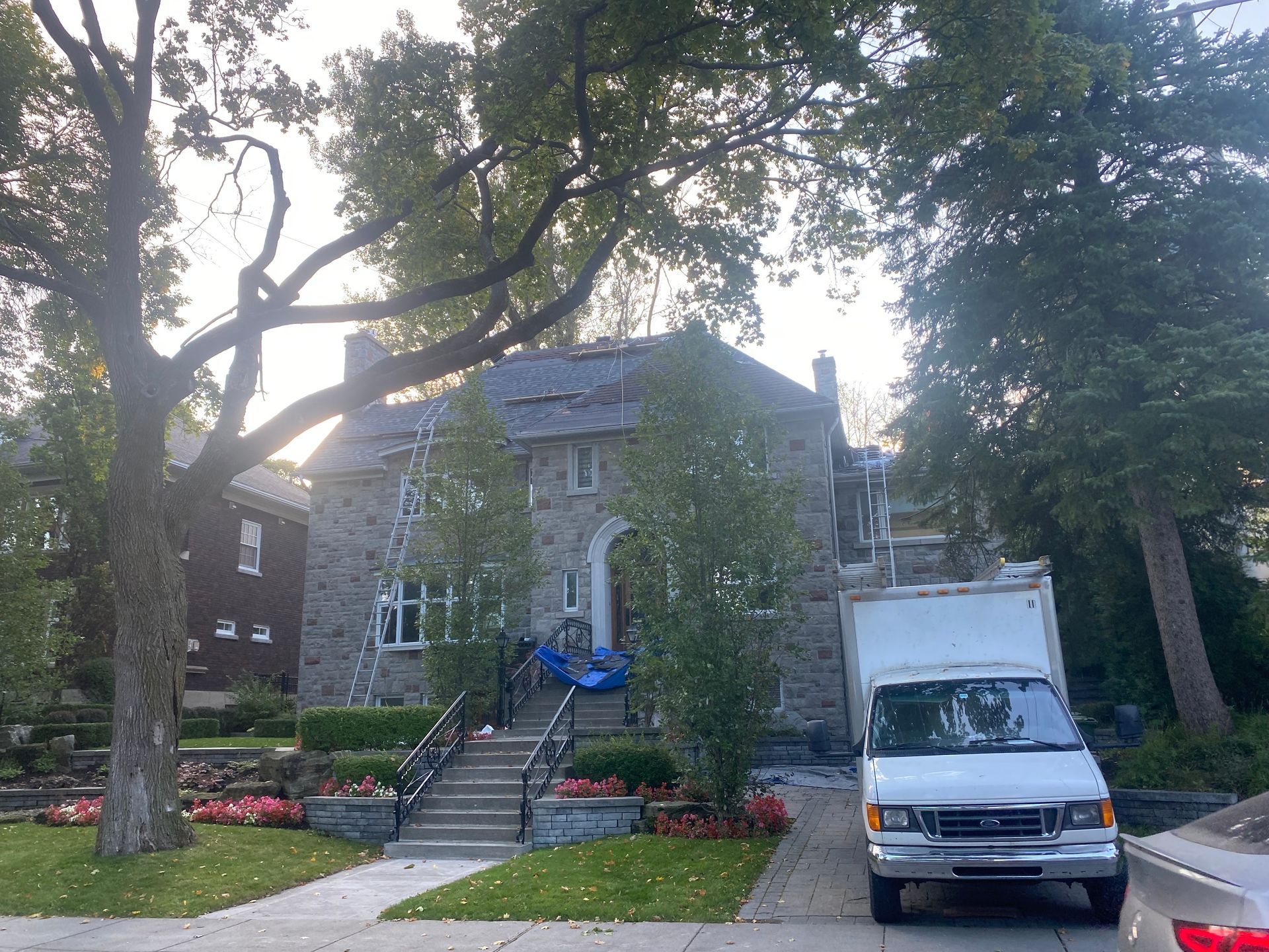Une camionnette blanche est garée devant une grande maison en pierre