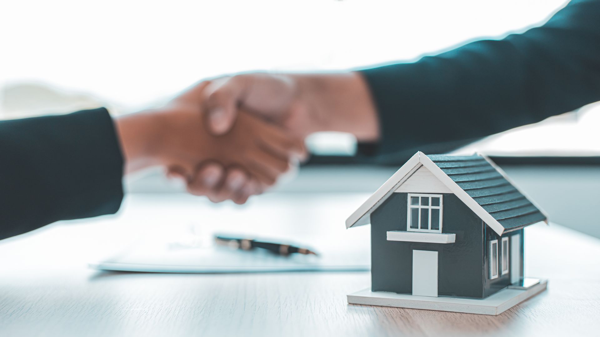 Two people are shaking hands over a table with a model house.