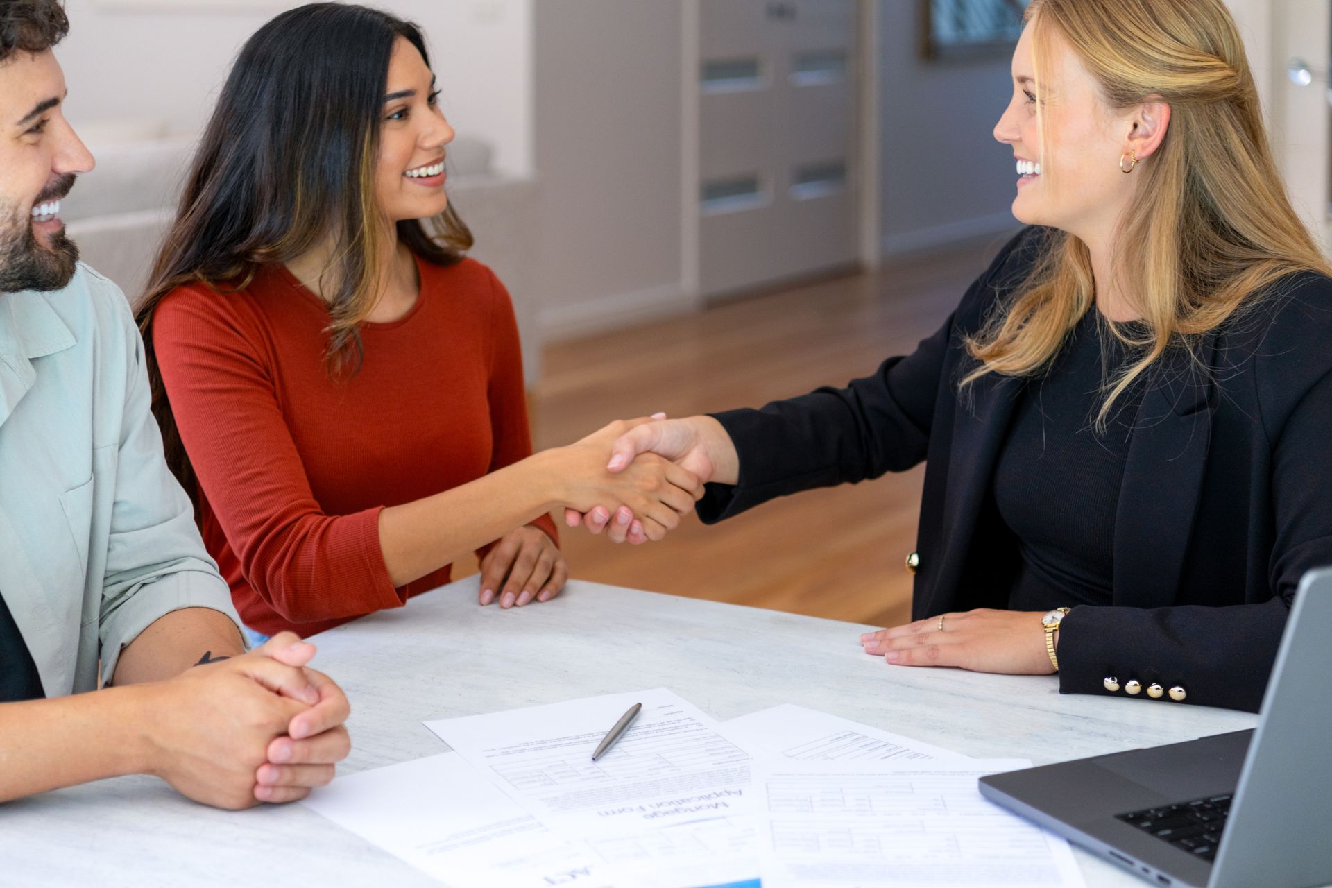 Two women shake hands during a business meeting discussing insurance agency services collaboration.