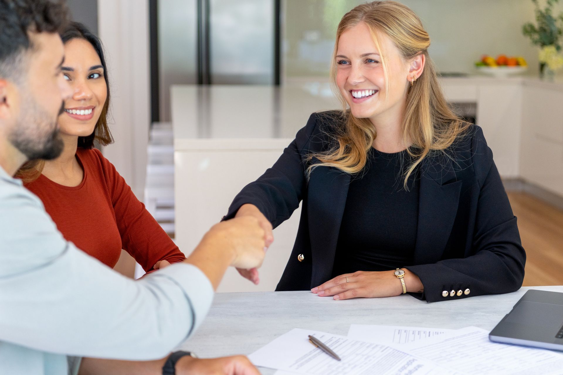 A woman and man shake hands during a business meeting discussing insurance agency services.