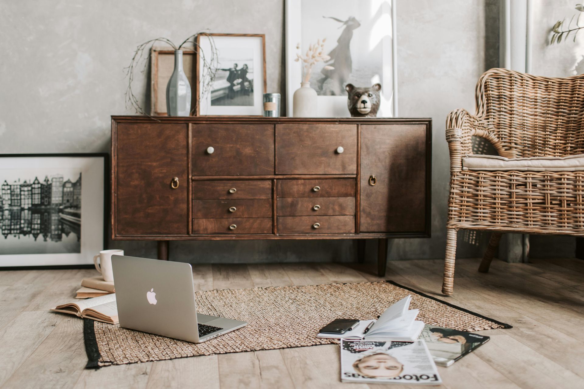 Wooden cabinet with decor, wicker chair, laptop on rug, and artwork.