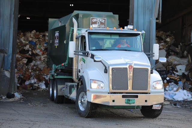 Orifice White and green garbage truck exiting a waste processing facility.