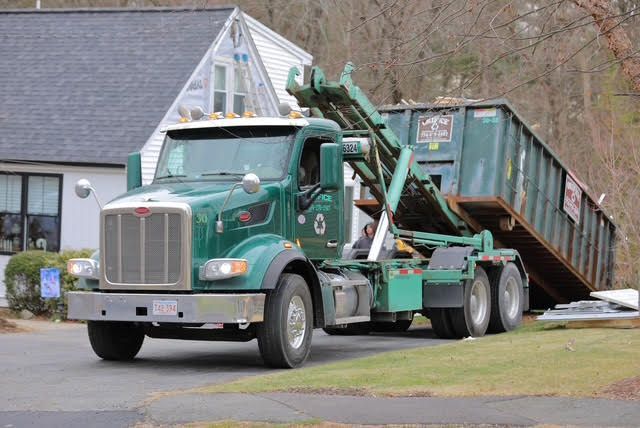 Green Orifice dump truck lowering a container in front of a building.