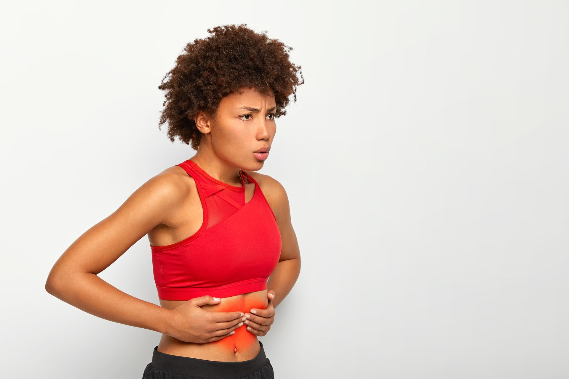 Woman in red sports bra holding her abdomen, showing pain, and looking concerned.