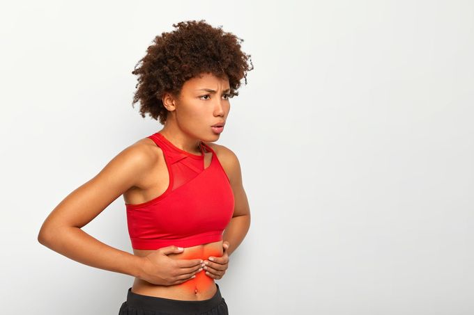 Woman in red sports bra holding her abdomen, showing pain, and looking concerned.