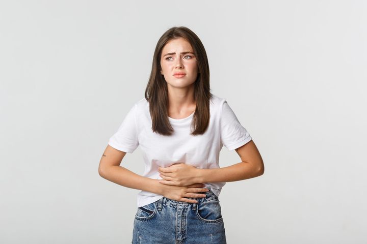 Woman in white shirt and jeans holding her stomach, looking distressed.