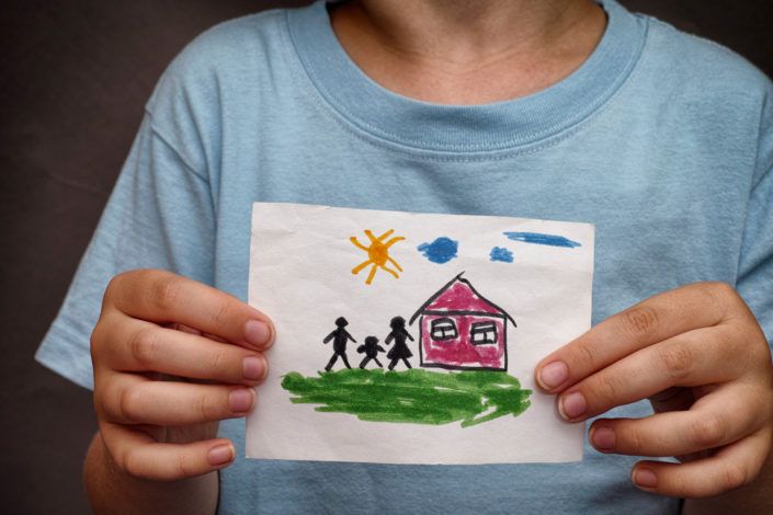 a child is holding a drawing of a family and a house