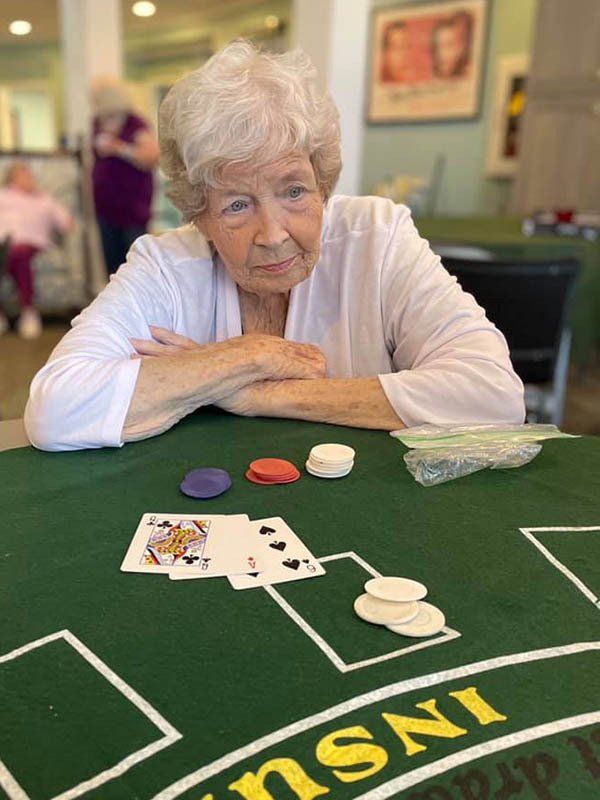 Woman at a table with cards and chips. She's looking at the cards. Green felt, various colored chips.