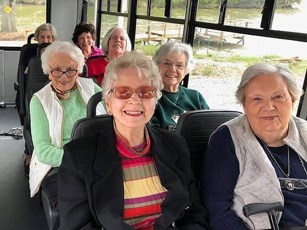 Group of older women smiling inside a vehicle, possibly a bus, near a body of water.