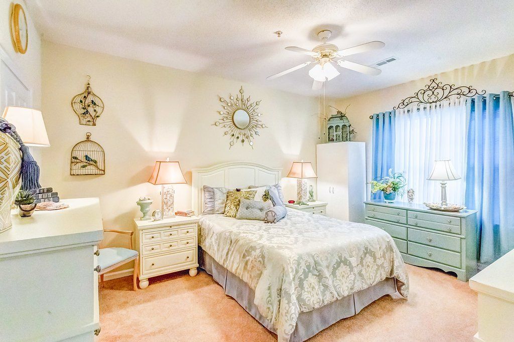 Bedroom with cream-colored walls, light blue furniture, bed with decorative bedding, and a ceiling fan.