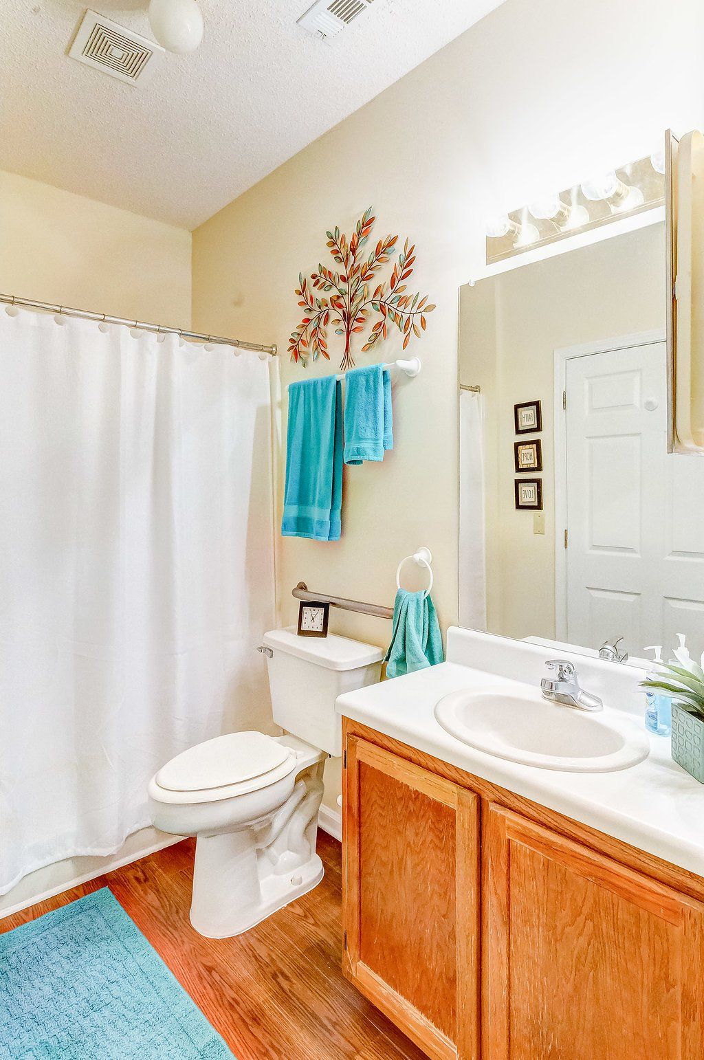 Bathroom with white shower curtain, teal towels, wooden cabinet, and mirror.