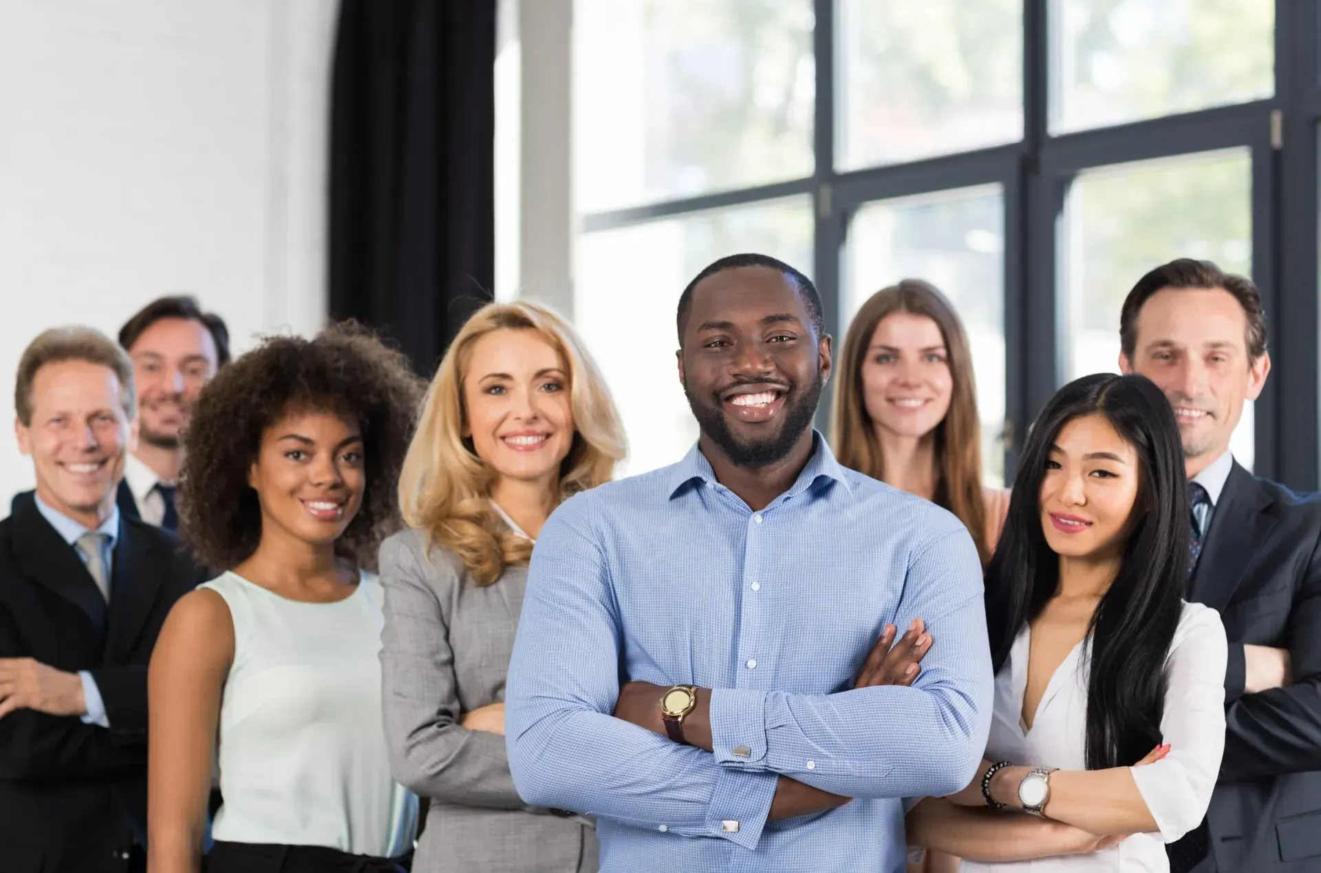 Group of diverse professionals smiling with arms crossed, in office setting.