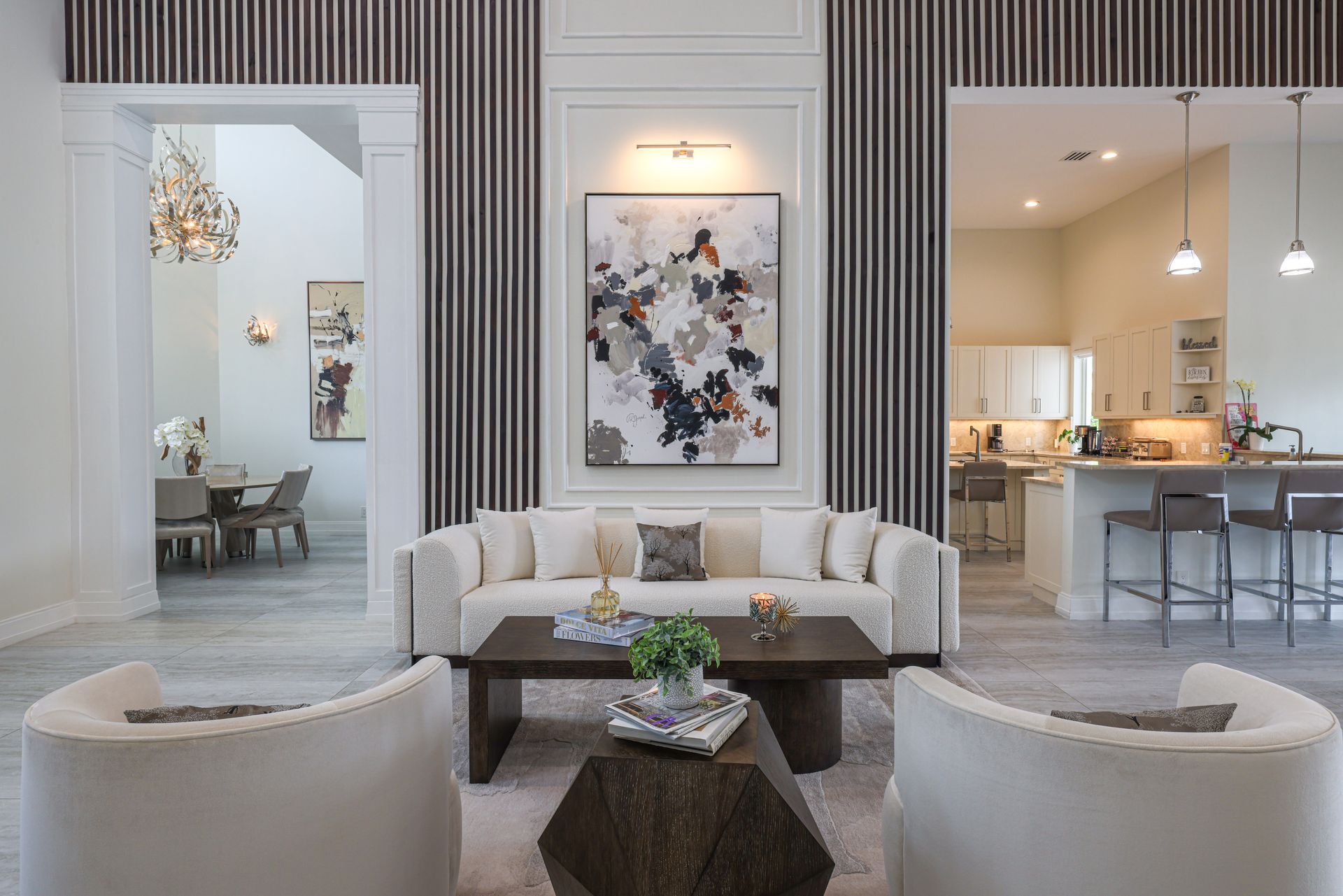 Living room with modern furniture, artwork, and kitchen in the background.