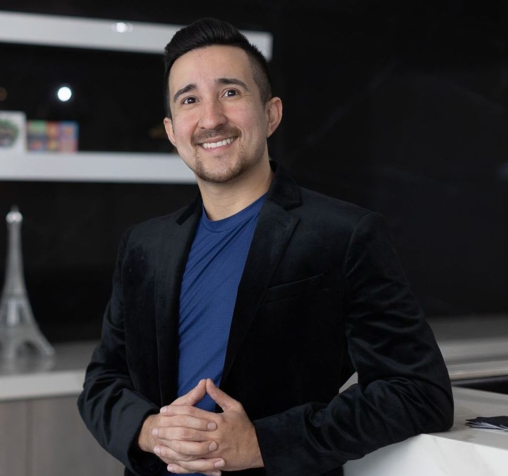 A man in a suit and a black shirt is smiling in a black and white photo.