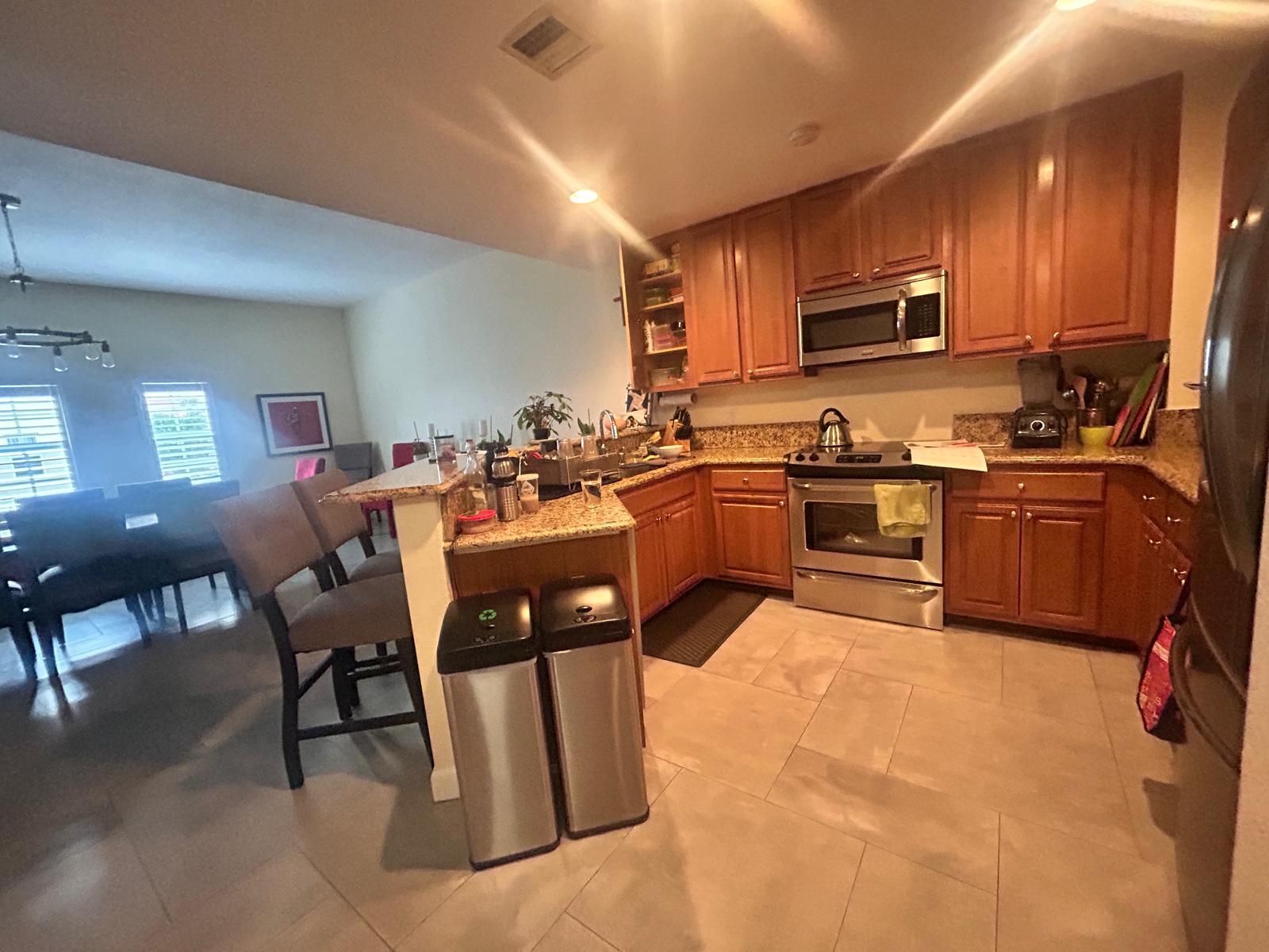 A kitchen with wooden cabinets and stainless steel appliances and a dining room in the background.