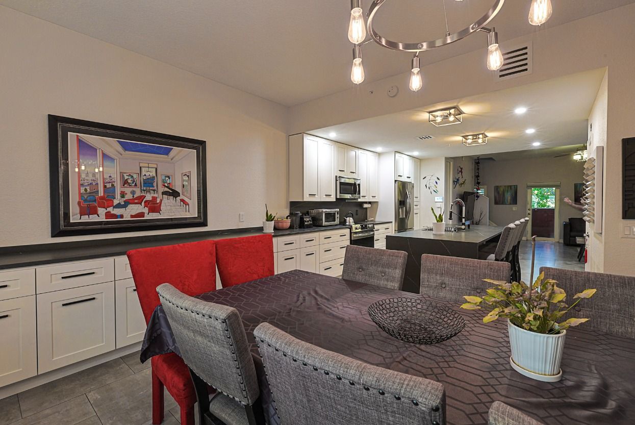 A dining room with a table and chairs and a kitchen in the background.