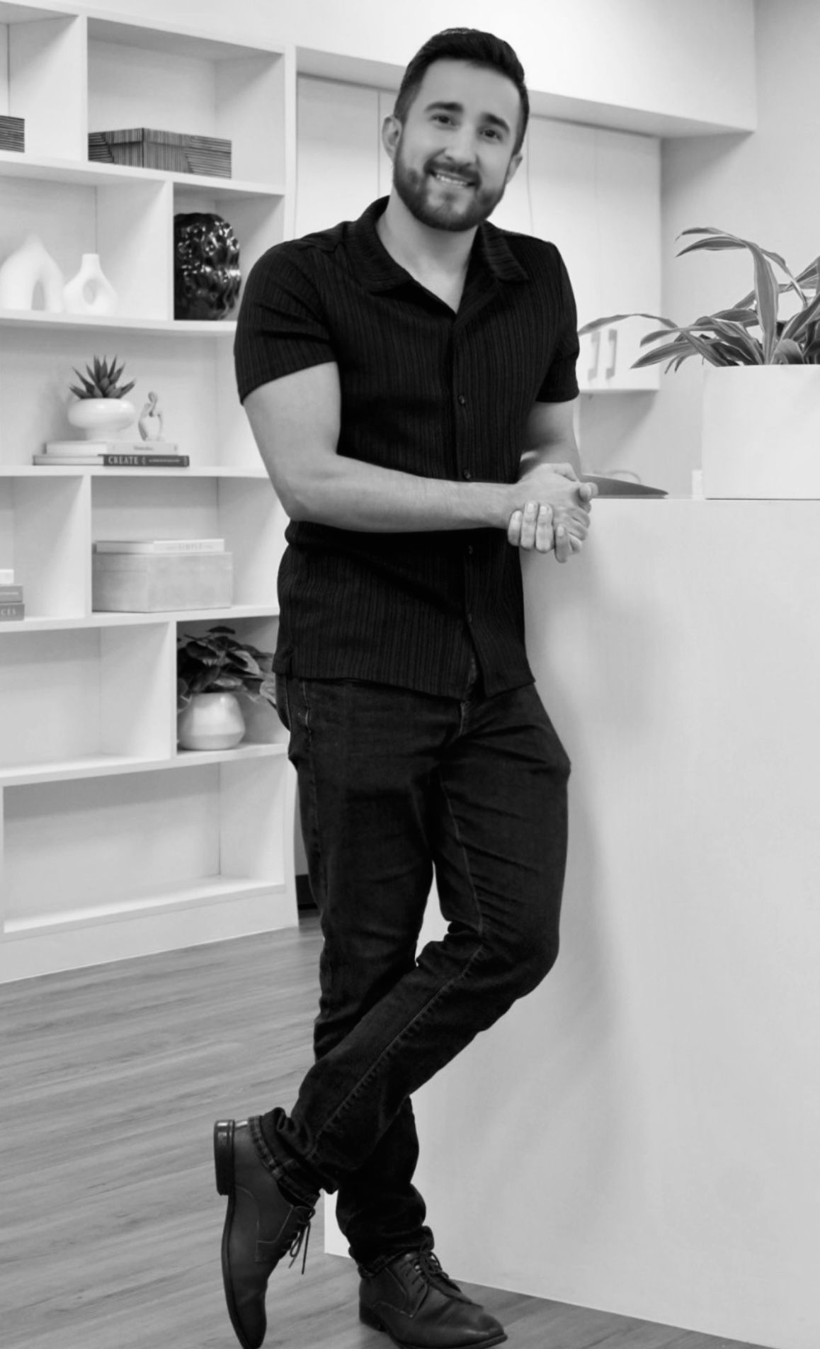 A man in a suit and a black shirt is smiling in a black and white photo.