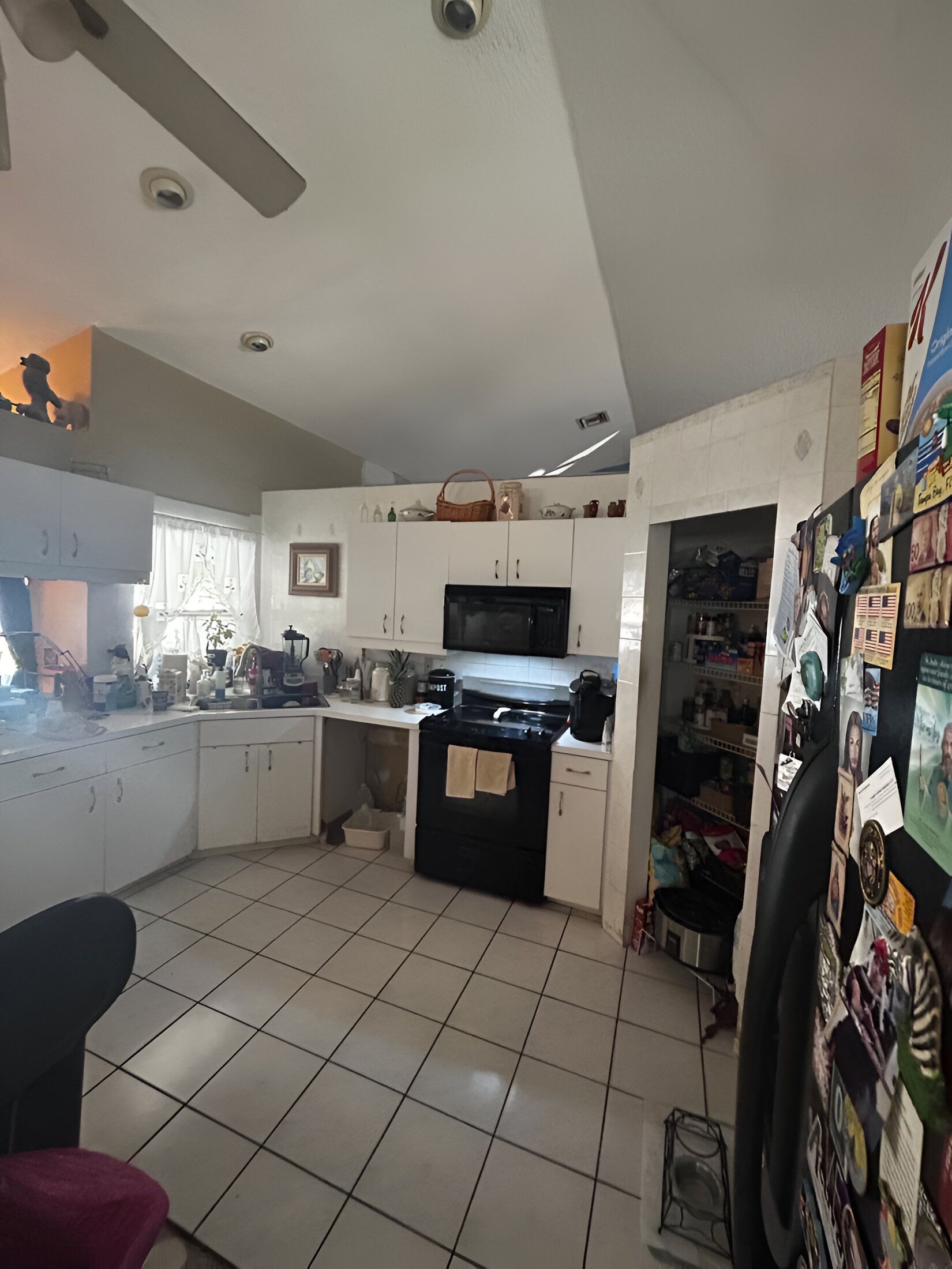 A kitchen with white cabinets , a black stove , a microwave , and a ceiling fan.