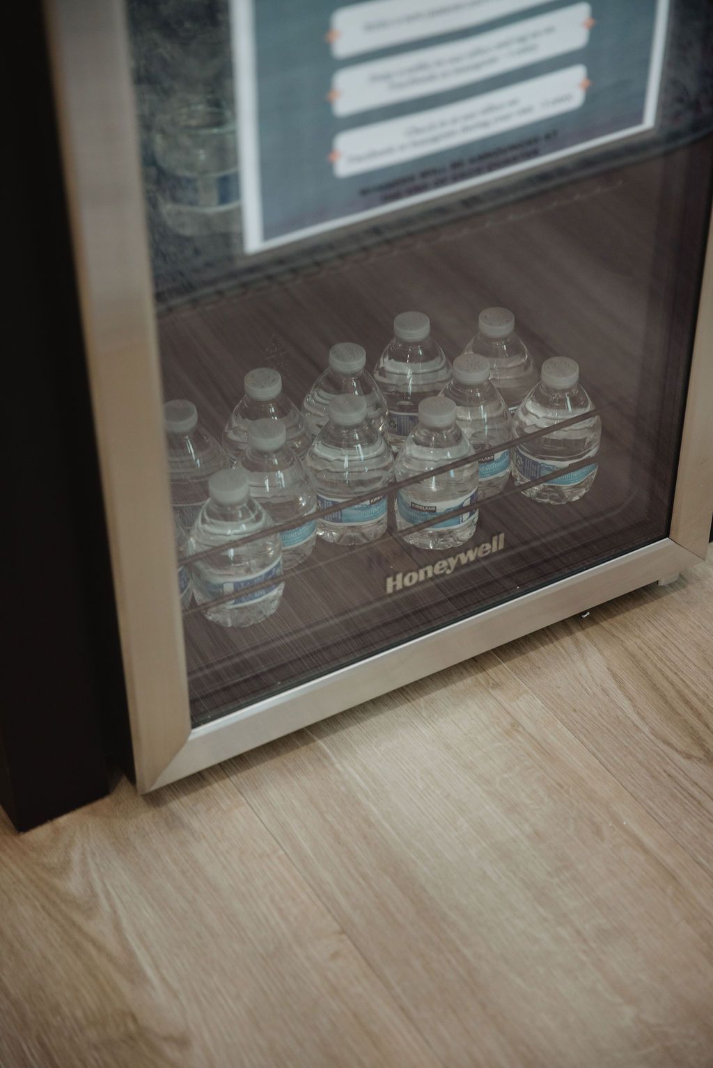 Mini-fridge with water bottles on shelves, wood-look floor.