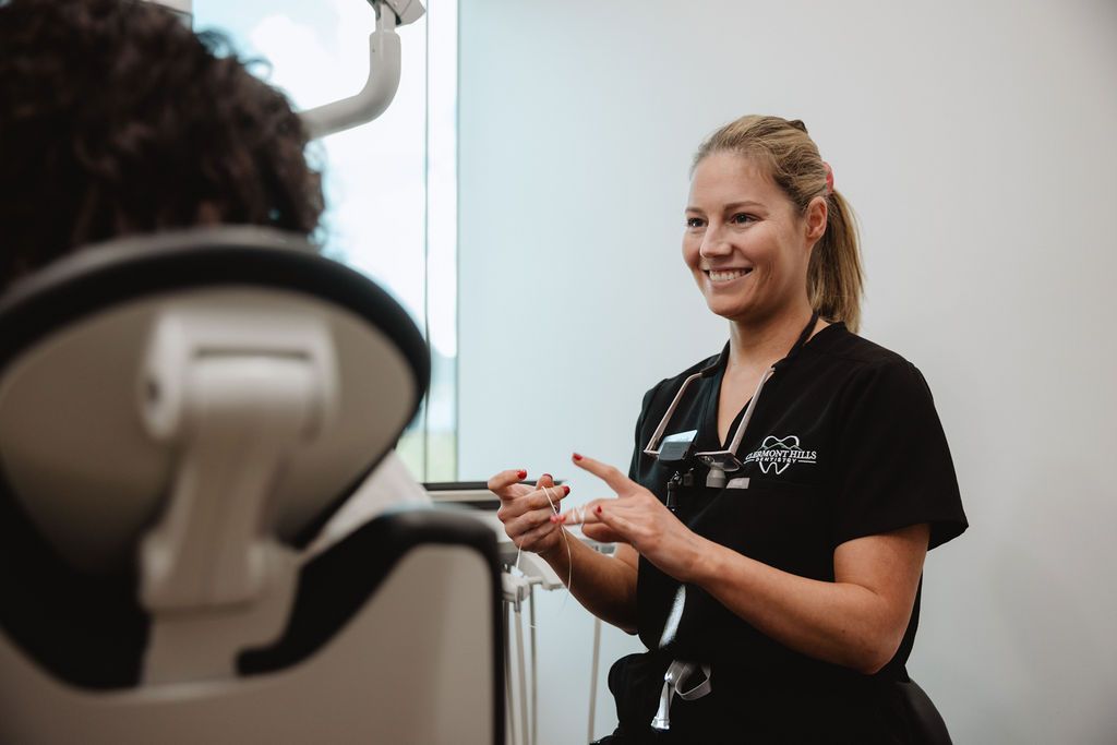 Dental professional in black scrubs, smiles while explaining something to a patient in a dentist chair.