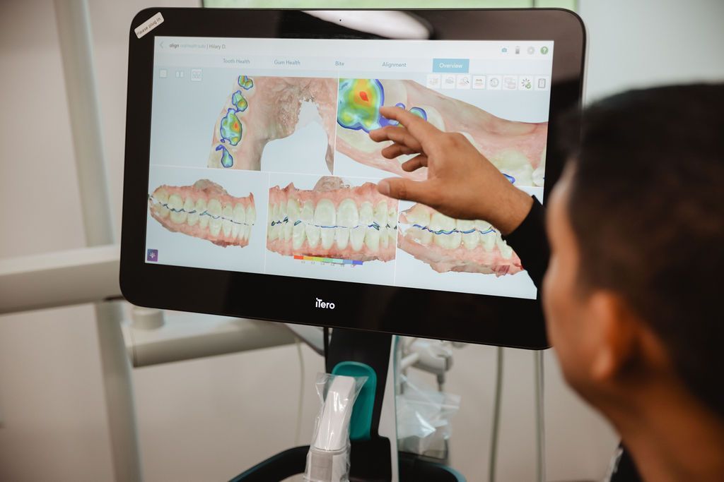 Person pointing at dental scan on a touch screen monitor. The scan shows teeth with color-coded analysis.
