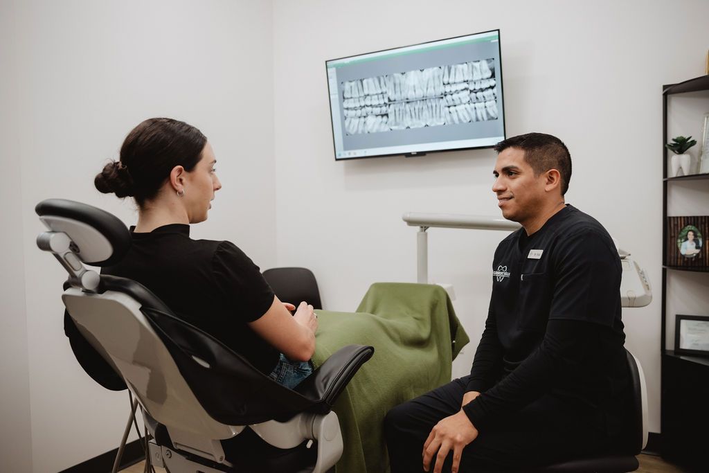 Dentist consulting with a patient in a dental office, reviewing X-rays on a monitor.