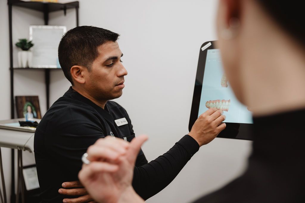 Man in black shirt pointing at tablet screen with someone else, indoors.