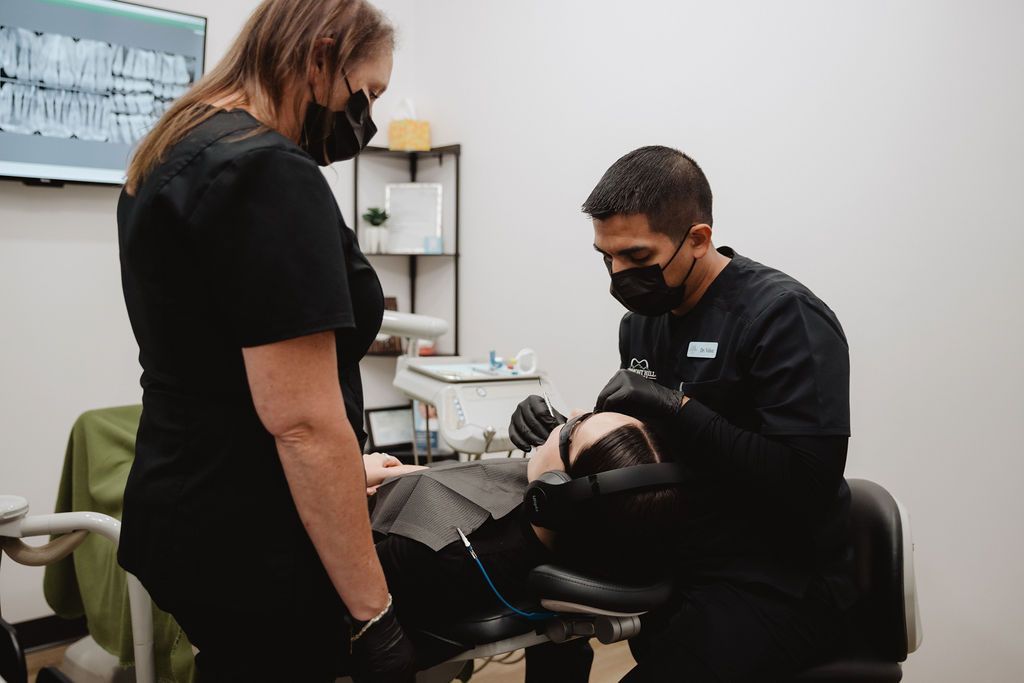 Dentist and assistant examining patient's teeth in a dental office. Both wearing masks and gloves.