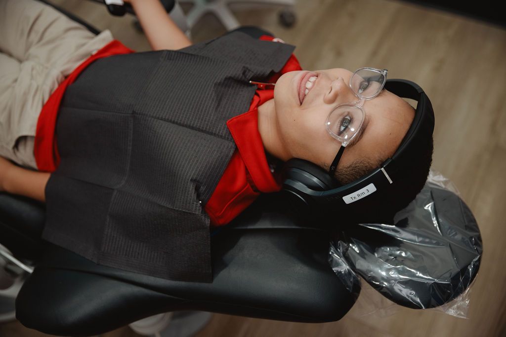 Person wearing headphones, glasses, and a bib, in a dental chair.