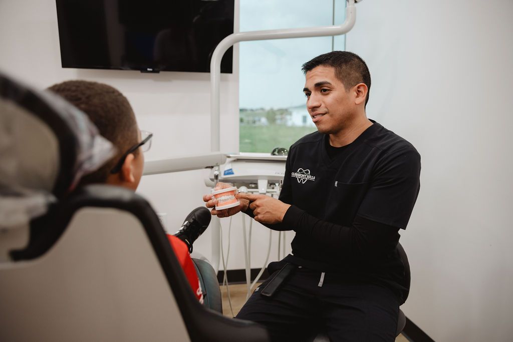 Dentist showing a young patient teeth model in dental office.