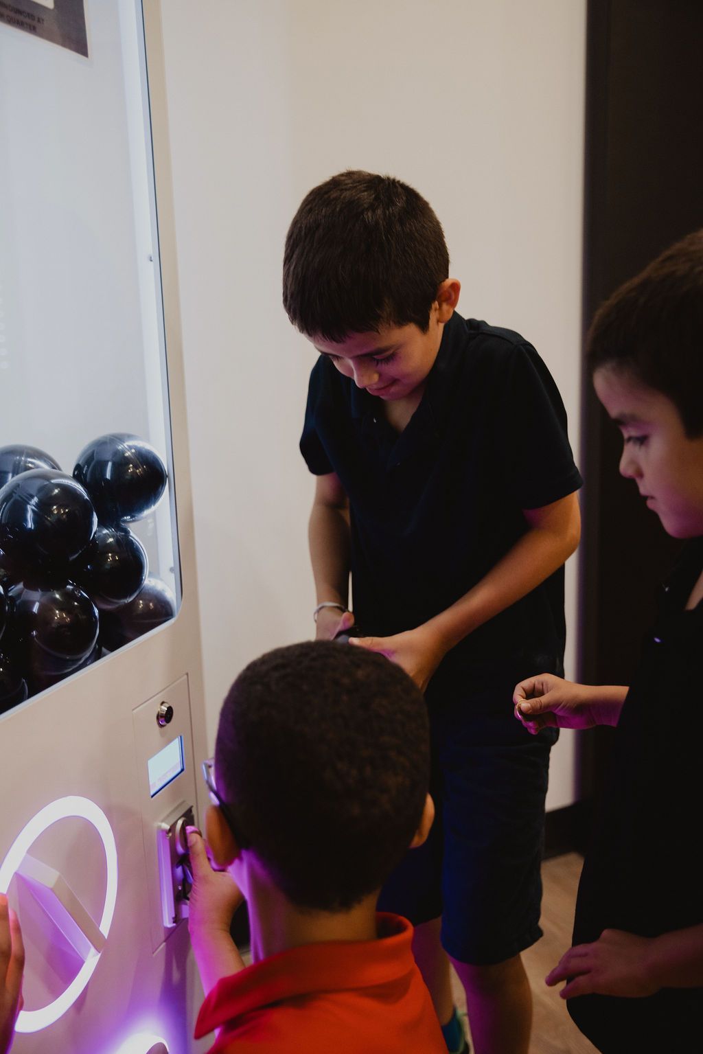 Three children playing a prize vending machine, focused on the controls and opening.