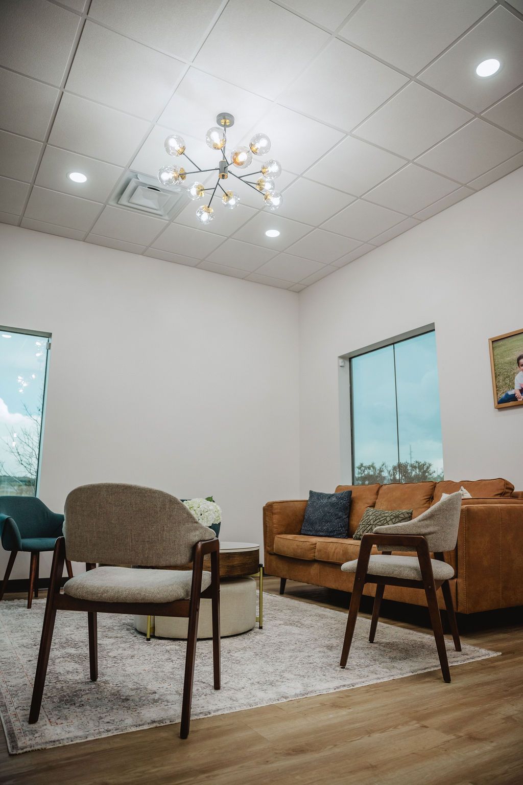 Bright, modern waiting room with a brown sofa, chairs, area rug, and a decorative chandelier.