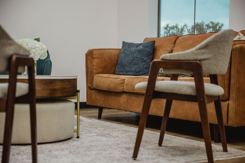 Cozy living room with a brown couch, two chairs, and a coffee table, with a window in the background.
