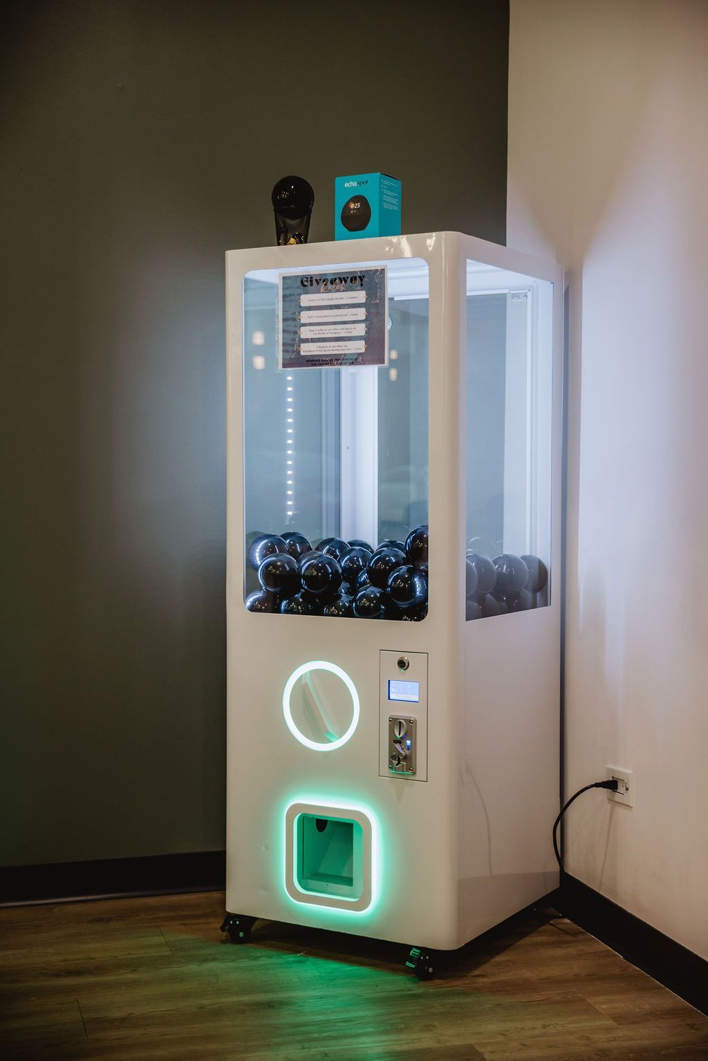 White prize machine with black balls, green and white lights. Black object and blue cube on top.