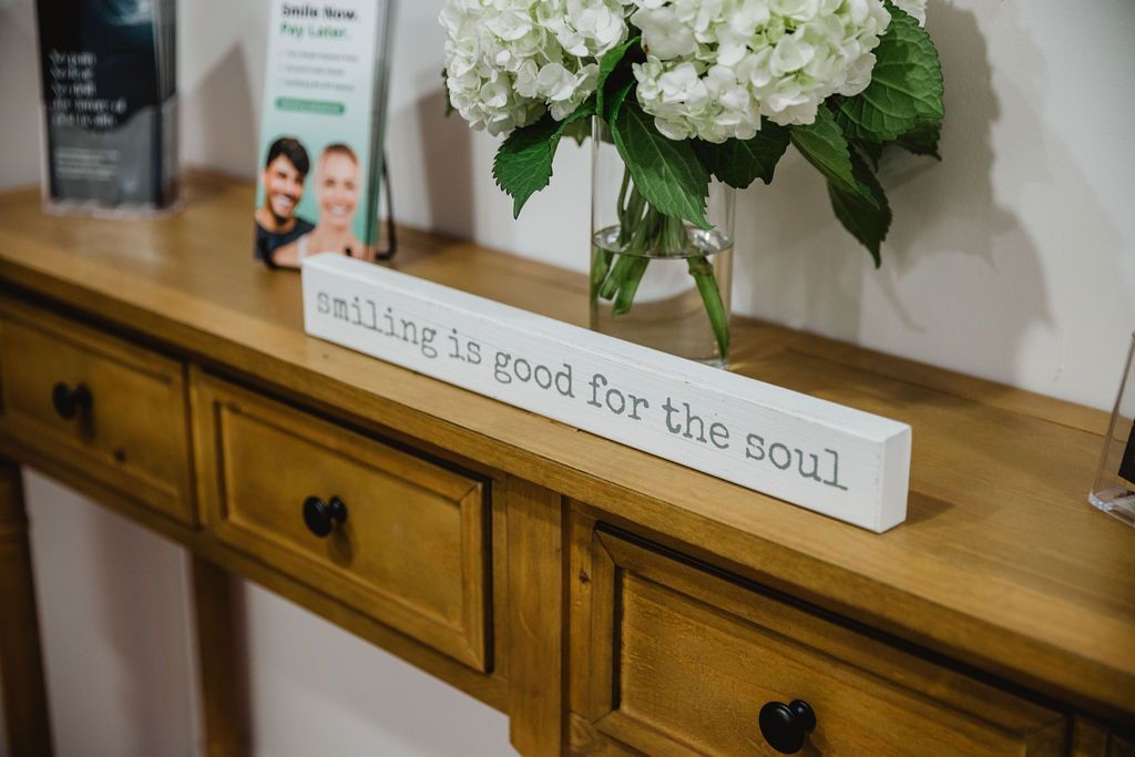 Wooden table with a vase of white flowers and a sign that says, 