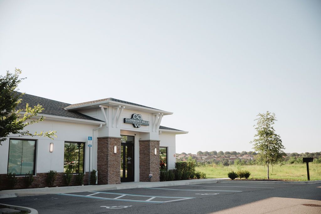 Exterior of a white building with a sign, brick columns, and a paved parking lot.